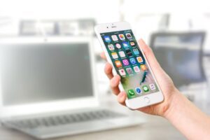 iOS 26 - Felhasználó a kezében tart egy fehér iPhone telefont egy laptop előtt